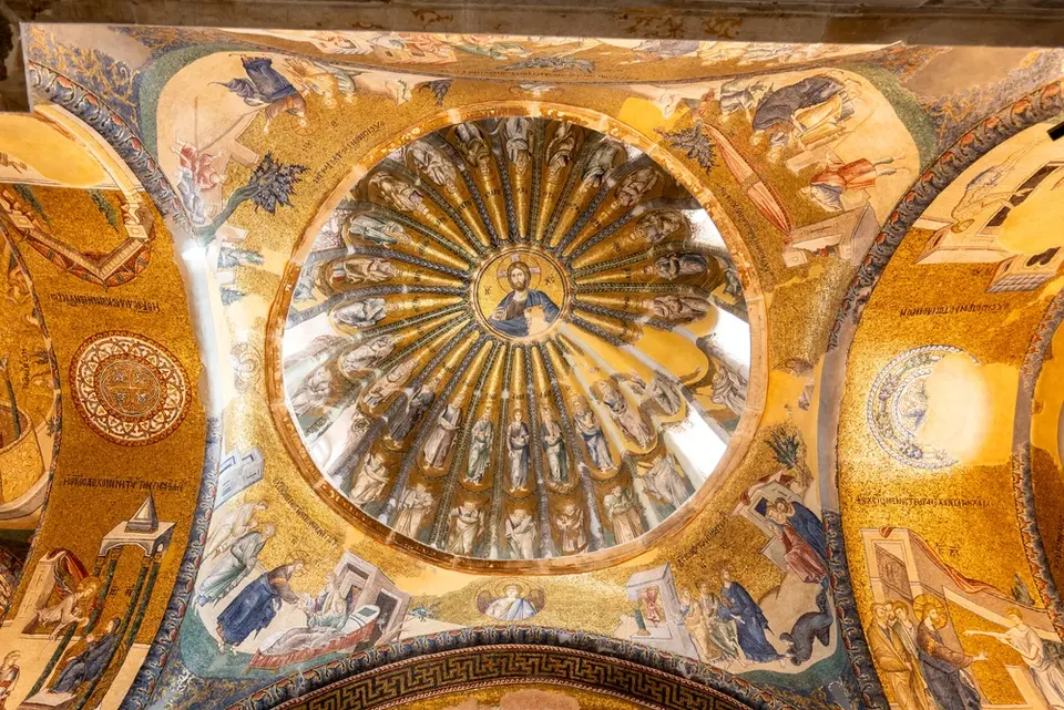 Looking up into a gold mosaic dome with a medallion of Christ at the centre and standing figures in the flutes around it